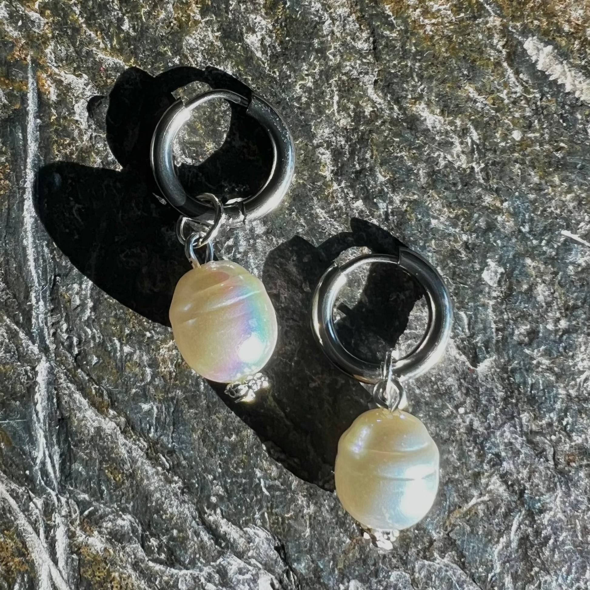 A pair of silver hoop earrings with pearl accents, displayed on a stone surface.