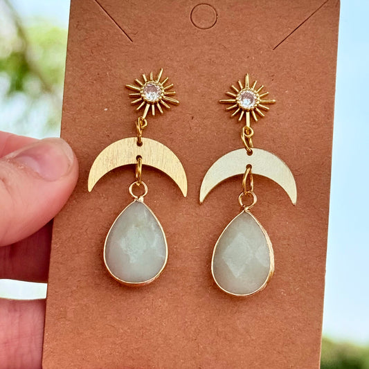 Pair of earrings on a brown card held by a hand with a blurred natural background