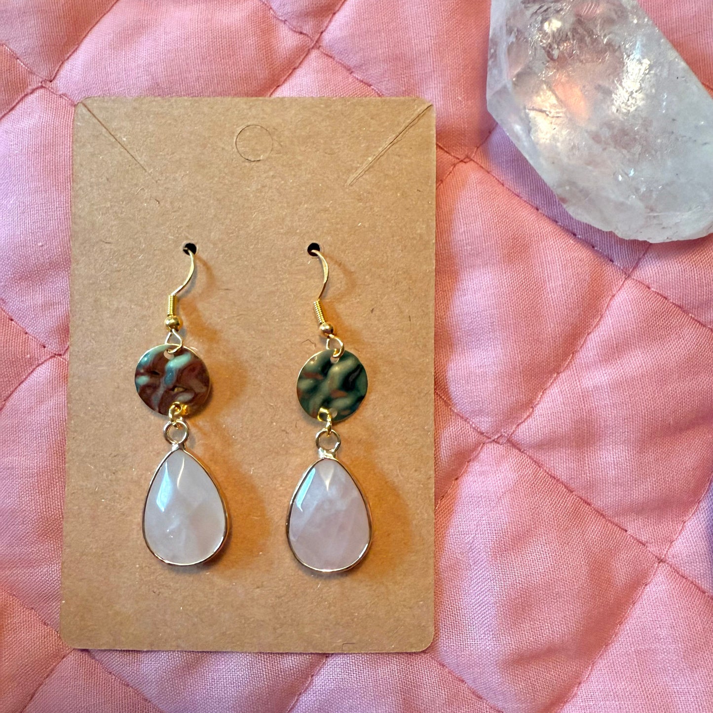 Pair of earrings on a cardboard backing with a pink quilted fabric background