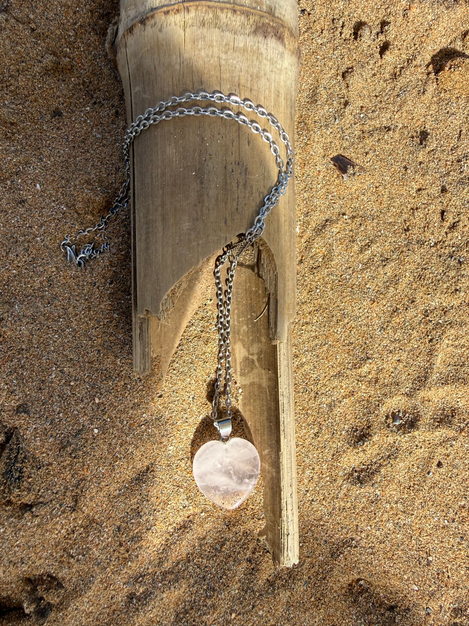 Necklace with a pendant on a piece of wood on sandy ground