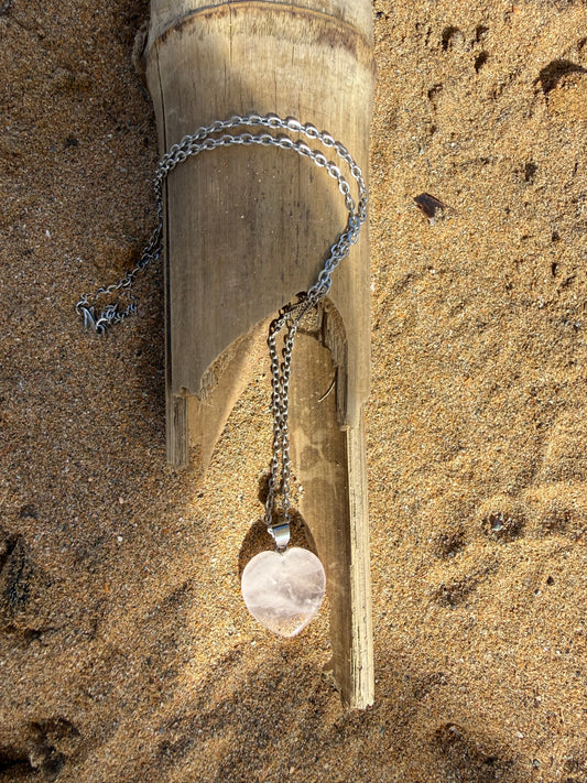 Necklace with a pendant on a piece of wood on sandy ground